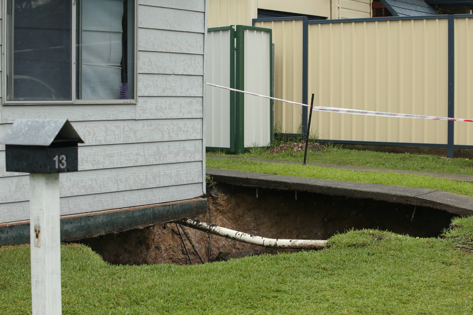 A sinkhole opened up in the front yard of a house, cordoned off with danger tape