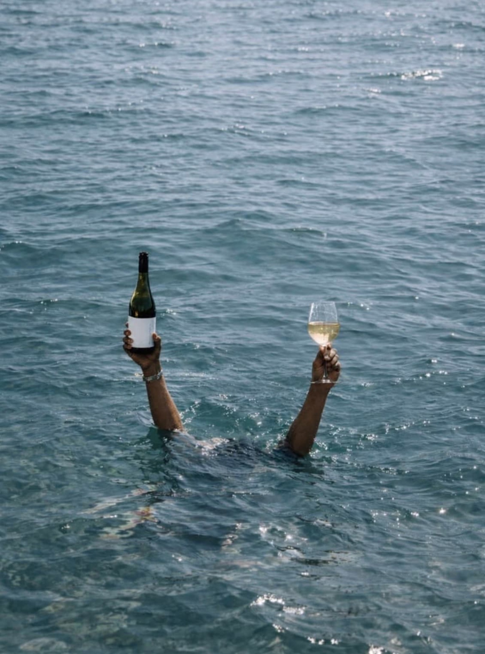 A swimmer in the surf off Newcastle holding up a bottle of wine and a full glass