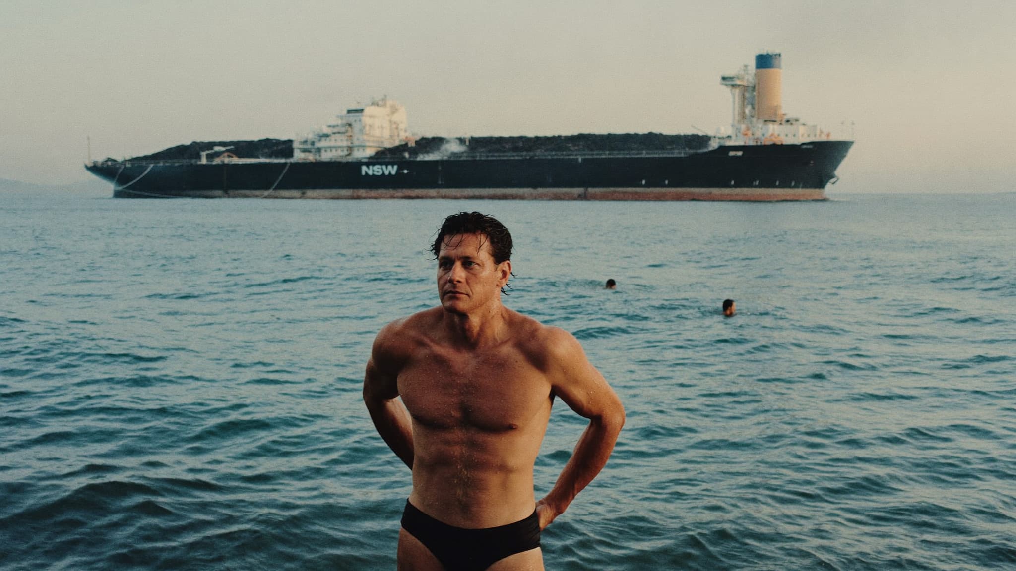 An ocean swimmer on a Newcastle beach with a laden coal ship offshore marked NSW, at dusk.