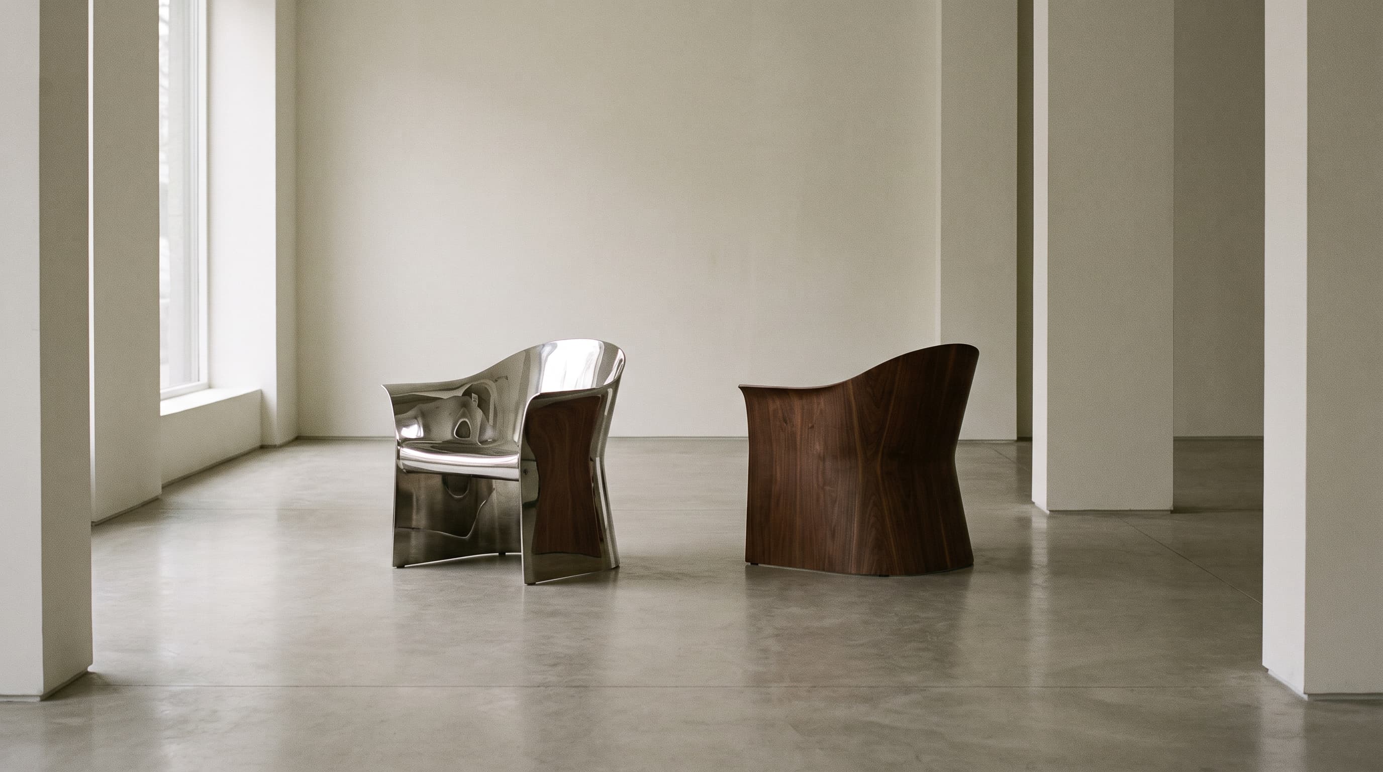 A minimalist concrete room with two chairs facing opposite directions: one polished chrome, one warm timber.